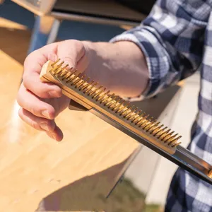 Detail view of a pizza oven cleaning brush with durable brass bristles and wooden handle.