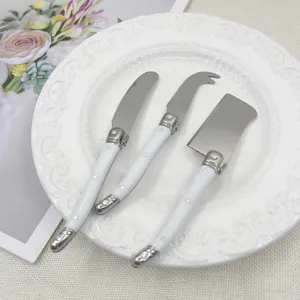 Three-piece stainless steel cheese knife set with white handles on a decorative white plate