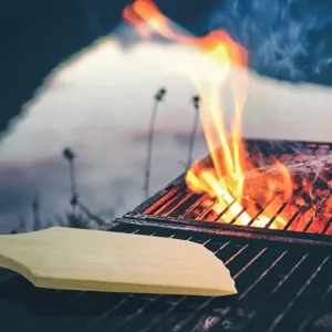 Vue détaillée d'un grattoir de nettoyage en bois pour barbecue sur des flammes vives