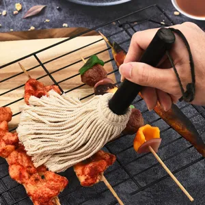 Action shot of a cotton basting mop applying sauce to skewers on a BBQ grill rack