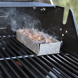 Primer plano de una caja ahumadora de acero inoxidable con astillas de madera en una parrilla