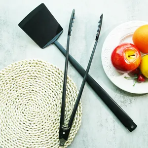 Black non-stick BBQ spatula and tongs set displayed with fresh fruits on marble