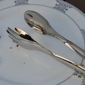 Detail view of polished stainless steel food tongs with spoon and fork design on a plate