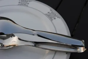 Macro view of polished silver stainless steel food tongs resting on a ceramic plate