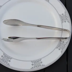 Professional polished stainless steel food tongs with spoon and fork design on a plate