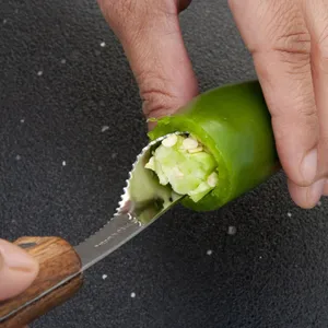 Close-up detail of stainless steel pepper corer with wood handle removing jalapeño seeds