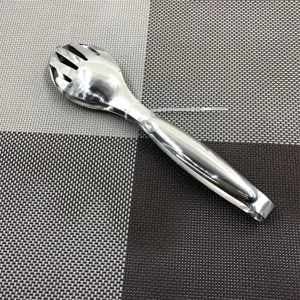 Detail of stainless steel food tongs with slotted design on a woven dining mat