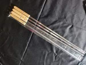 Nahaufnahme von vier Edelstahl-Grillspießen mit Eichenholzgriffen auf schwarzem Stoff.