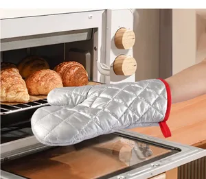 Close-up of a silver quilted oven mitt with red trim being used with a kitchen oven.