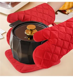 Red quilted oven mitts holding a black ceramic pot with gold handle in a kitchen setting