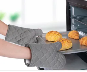 Grey quilted silicone heat-resistant oven mitts handling a fresh baking tray with bread