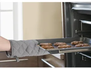 Action shot of grey quilted oven mitt removing fresh cookies from a hot oven