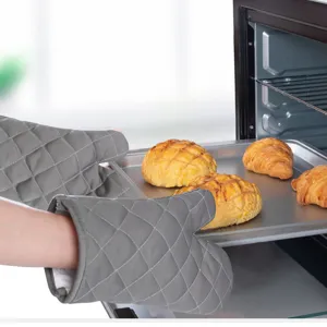 Grey quilted heat resistant oven mitts holding a baking tray with fresh bread