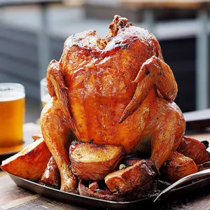 Succulent roasted whole chicken on a stainless steel BBQ roaster rack with crispy potatoes
