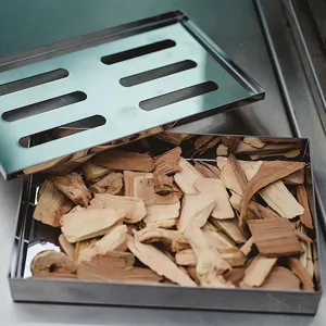 Close-up of stainless steel smoker box filled with natural wood chips for BBQ flavor