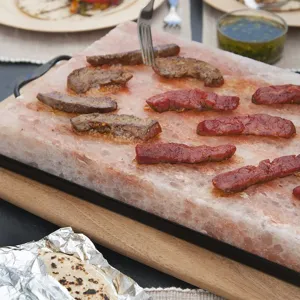 Nahaufnahme von Fleisch, das auf einem rosa Himalaya-Salzblock mit schwarzem Halter grillt.