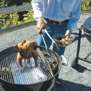 Detail view of a whole chicken grilling on a stainless steel BBQ beer can roaster rack