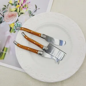 Detailed view of three stainless steel cheese knives with wood-grain handles on a white plate