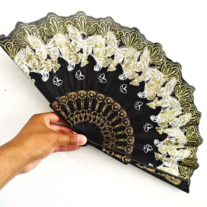 Detalle de un abanico plegable negro con motivos de mariposas doradas sostenido a mano
