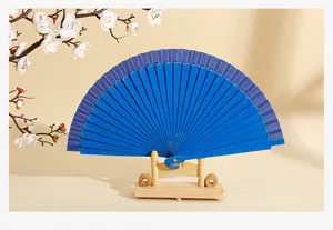 Detalle de un abanico plegable azul liso sobre un soporte de madera con flores blancas