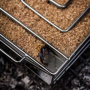 Close-up view of stainless steel smoker box with burning wood chips and smoke