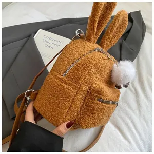 Detalle de mochila de felpa marrón con orejas de conejo y un suave pompón blanco.