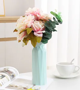 Vaso geometrico nordico in plastica azzurra con rose rosa su un tavolo luminoso