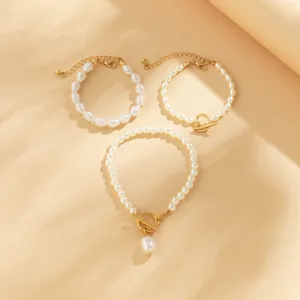 Elegante set di tre braccialetti di perle barocche con ciondoli a cuore d'oro su sfondo caldo