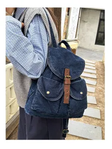Model wearing a vintage blue denim backpack with brown leather strap in outdoor setting