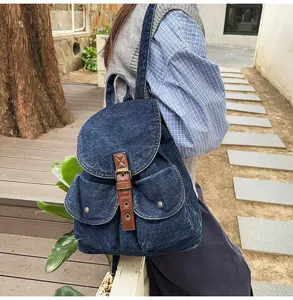 Side view of a vintage dark blue denim backpack with brown leather buckle straps.