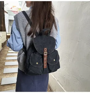 Black denim backpack for women with brown leather strap detail, worn in outdoor setting