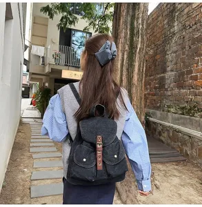 Stylish black denim backpack with leather buckle detail worn by a girl in city street