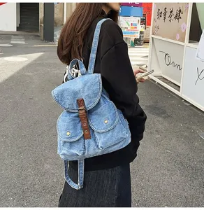 Close-up detail shot of a stylish denim backpack featuring a brown leather strap
