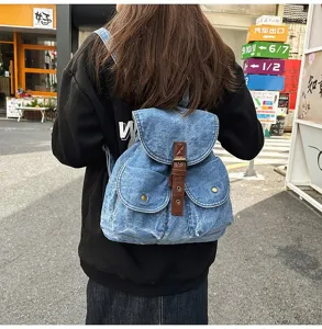 Blue denim backpack with brown leather buckle strap detail worn on model's back