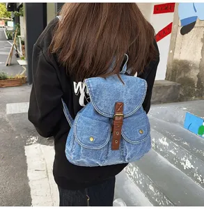 Casual light blue denim backpack with brown buckle straps shown in a street style view