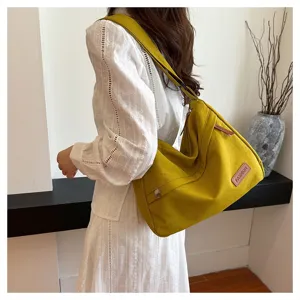 Grand sac bandoulière en toile jaune moutarde porté par un mannequin en robe blanche