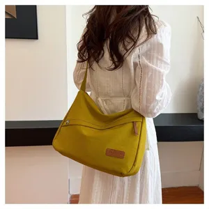 Grand sac bandoulière jaune moutarde porté par un mannequin en robe blanche longue