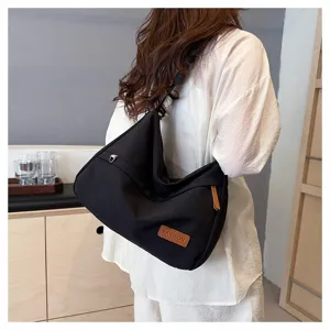 Vue latérale détaillée d'un grand sac à bandoulière en toile noire porté par un mannequin