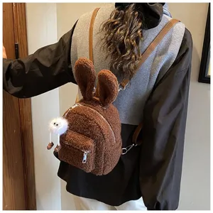 Mochila de peluche marrón con orejas de conejo y colgante de monstruo blanco en la espalda