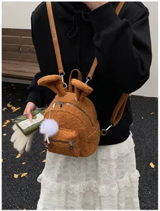 Vista detallada de la mochila de peluche marrón con orejas de conejo y pompón en un modelo.