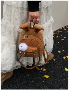 Primer plano de una linda mini mochila de felpa marrón con orejas de conejo y dije