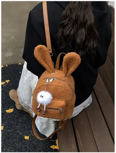 Vista trasera de una linda mochila de felpa de conejo marrón con orejas y un colgante de pompón