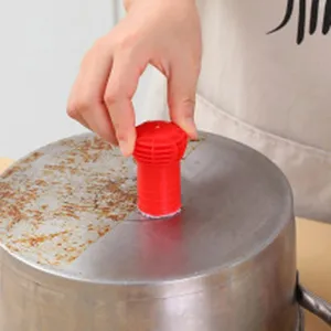 Close-up of a red handheld steel wire scrubber cleaning a burnt rusty metal pot bottom