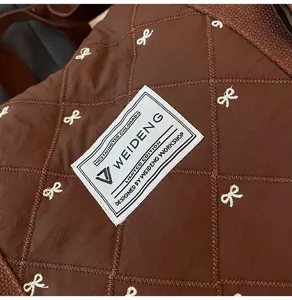 Brown quilted travel handbag detail, white bow embroidery, lightweight fashion design.