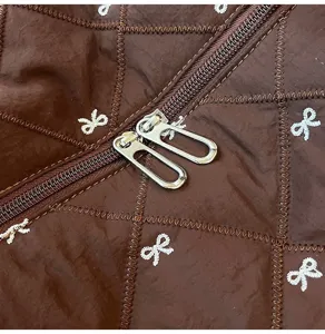 Brown quilted travel bag detail featuring white embroidered bows and metal dual zippers.