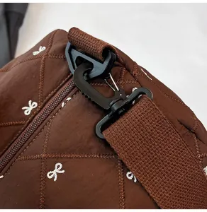 Close-up detail of brown quilted travel bag with black hardware buckle and white bow embroidery.
