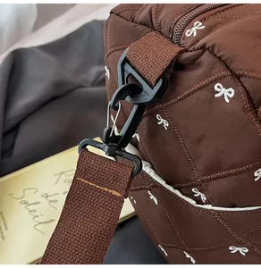 Close-up of brown quilted travel bag with cute embroidered bows and sturdy strap hook.