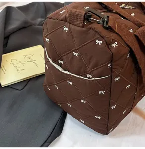 Detailed shot of brown quilted travel duffel bag with white bow embroidery and straps.