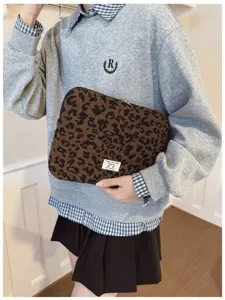 A lifestyle detail shot of a stylish leopard print laptop sleeve held by a model.