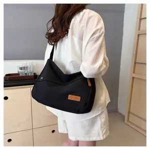 Grand sac à bandoulière noir minimaliste en toile porté par un mannequin sur l'épaule